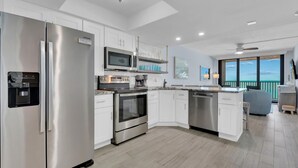 A modern kitchen with stainless steel appliances, white cabinetry, and a large window offering a view of the ocean. - SEA WINDS 504 - Direct Gulf Views from Coastal Renovated Beachfront Condo! (Marco Island)