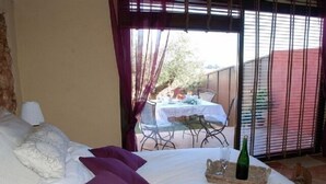 A bedroom with a bed, a table with chairs outside, and a bottle on the bed.