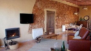 A cozy living room with a fireplace, stone wall, wooden furniture, and a television.