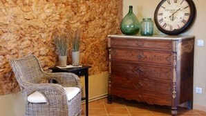 A wicker chair with a cushion, a wooden dresser with drawers, and a wall clock.