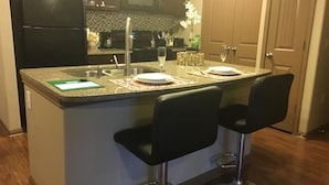 Une cuisine dotée d’un îlot central, de deux tabourets de bar, d’un four à micro-ondes et d’un réfrigérateur.