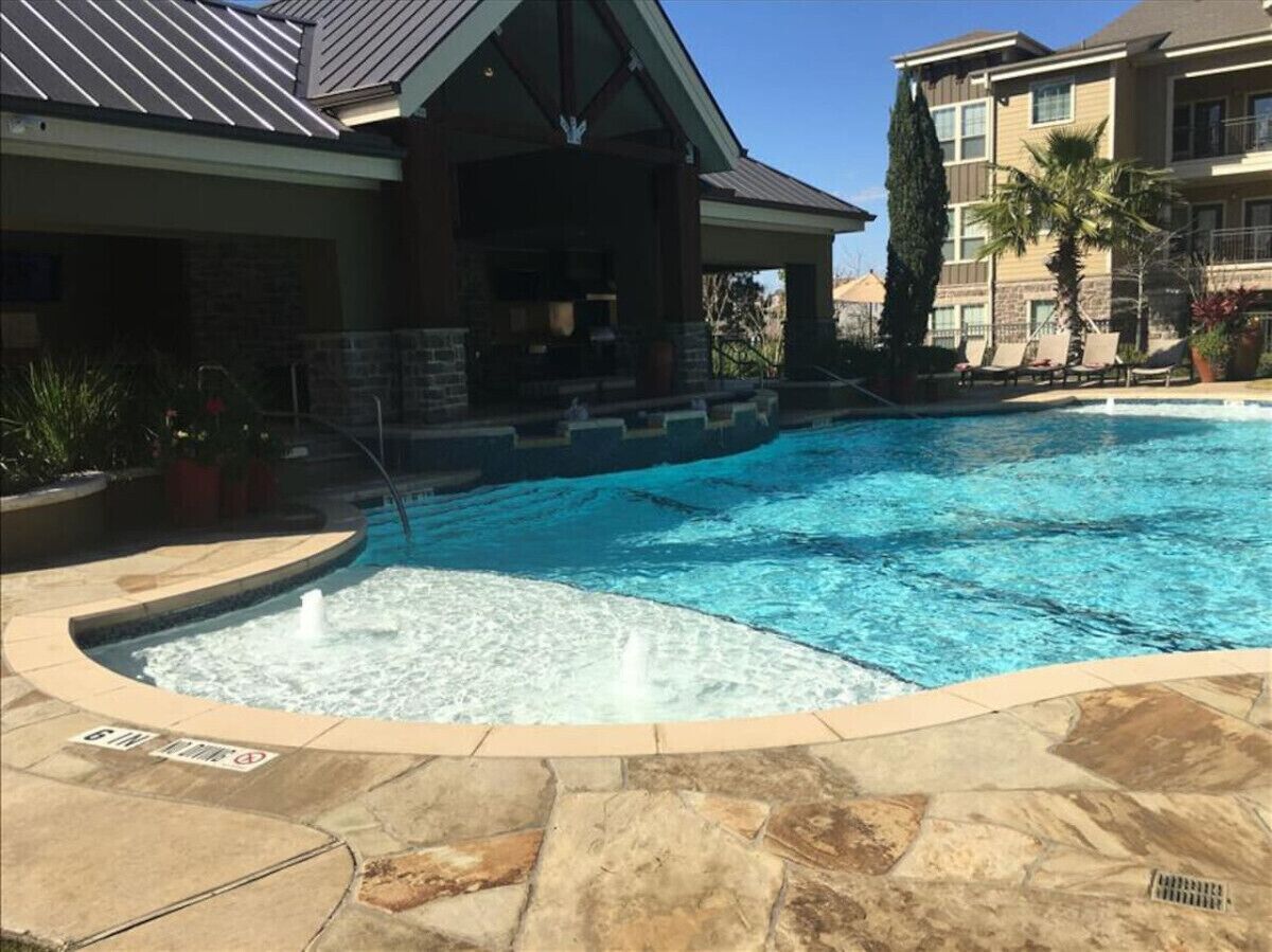 Ein Schwimmbecken mit Whirlpool, umgeben von Steinfliesen und einem Gebäude mit Schrägdach.
