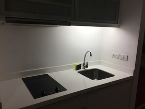 A kitchen with a white countertop, a black sink, a stainless steel faucet, and a black induction cooktop.