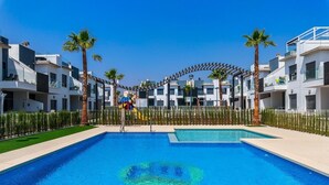 A swimming pool with a clear blue center, surrounded by modern buildings and palm trees.