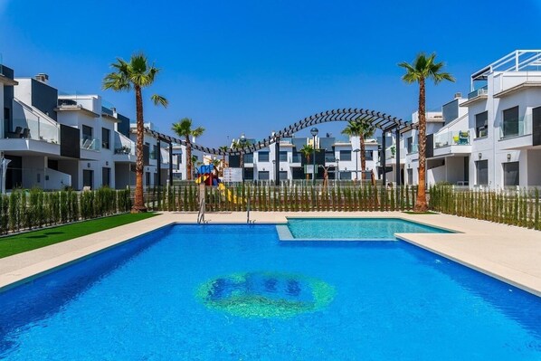A swimming pool with a clear blue center, surrounded by modern buildings and palm trees.