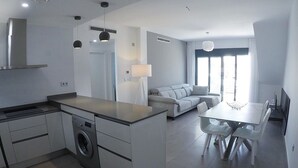 A modern kitchen with a built-in washing machine, a dining area with a table and chairs, and a living area with a sofa and a TV.