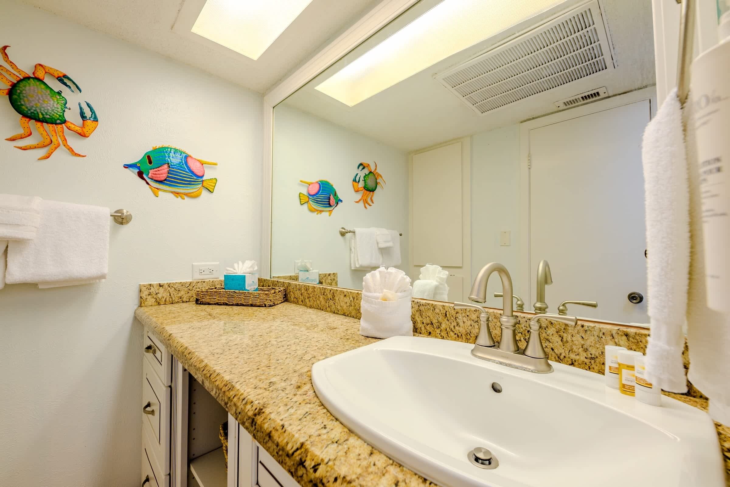 Un baño con encimera de granito, lavamanos, espejo y decoración de peces en la pared.