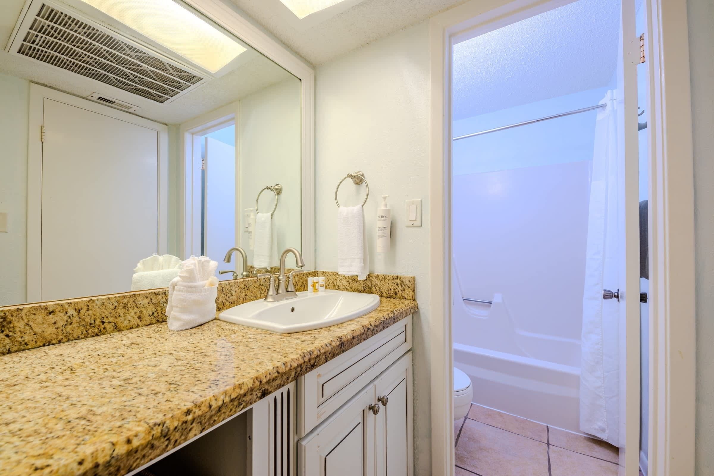 A bathroom with a granite countertop, a sink, a mirror, and a shower area.