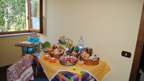 A dining table with a yellow tablecloth, various food items, and a window with a view of trees. - "Il gelsomino del Perugino" home with garden, a stone's throw from the center.  (Città della Pieve)