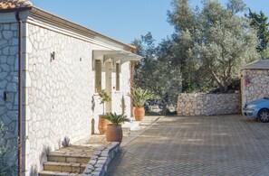 A stone building with a covered porch, a paved driveway, and a car parked nearby.