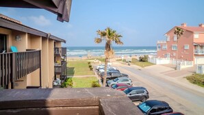 A coastal hotel with a view of the ocean, a parking lot with cars, and a palm tree. - Cranes Cove Tranquil (South Padre Island)