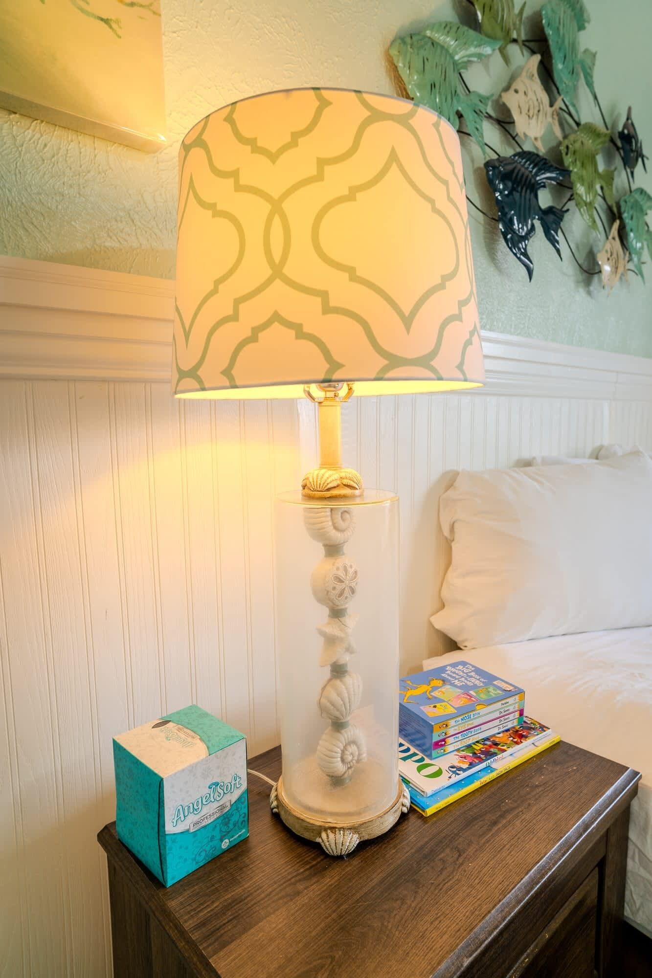 Een nachtkastje met een lamp, zakdoekjes en een stapel kinderboeken.