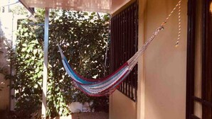 A hammock hanging between two poles in a covered outdoor area with a view of a garden and a building. - Country meets beach! Las Palmitas Costa Rica (Palmar Norte)