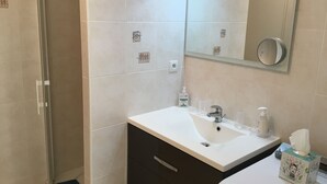 A bathroom with a white sink, a mirror, and a toilet. There are two bottles of hand sanitizer and a tissue box on the sink.