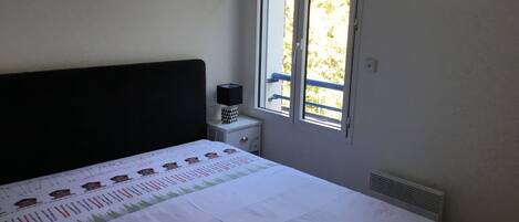 A bedroom with a bed, a nightstand, a window, and a radiator.