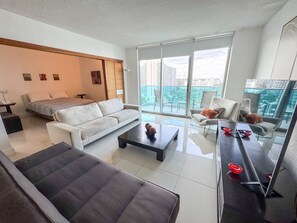 Een moderne hotelkamer met een bed, een bank, een salontafel en een balkon met uitzicht op de stad.