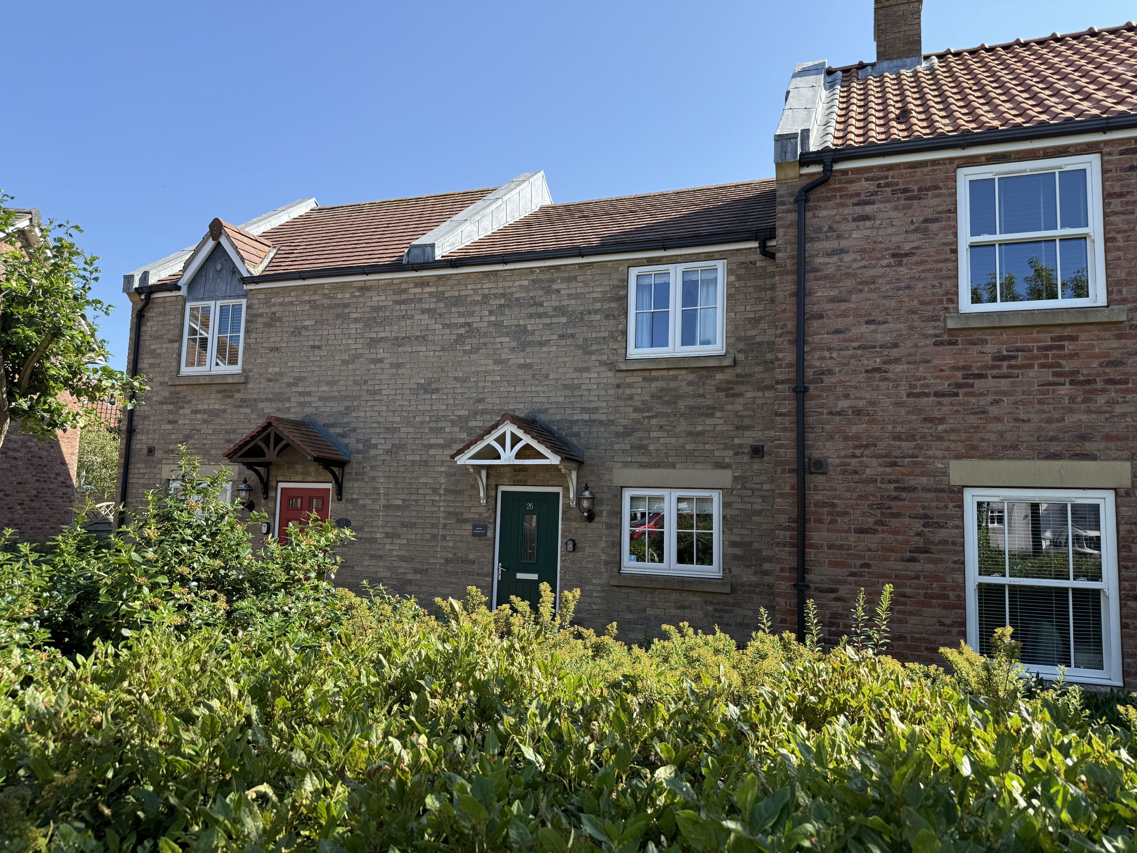 A two-story brick house with a green door, white-framed windows, and a red door.