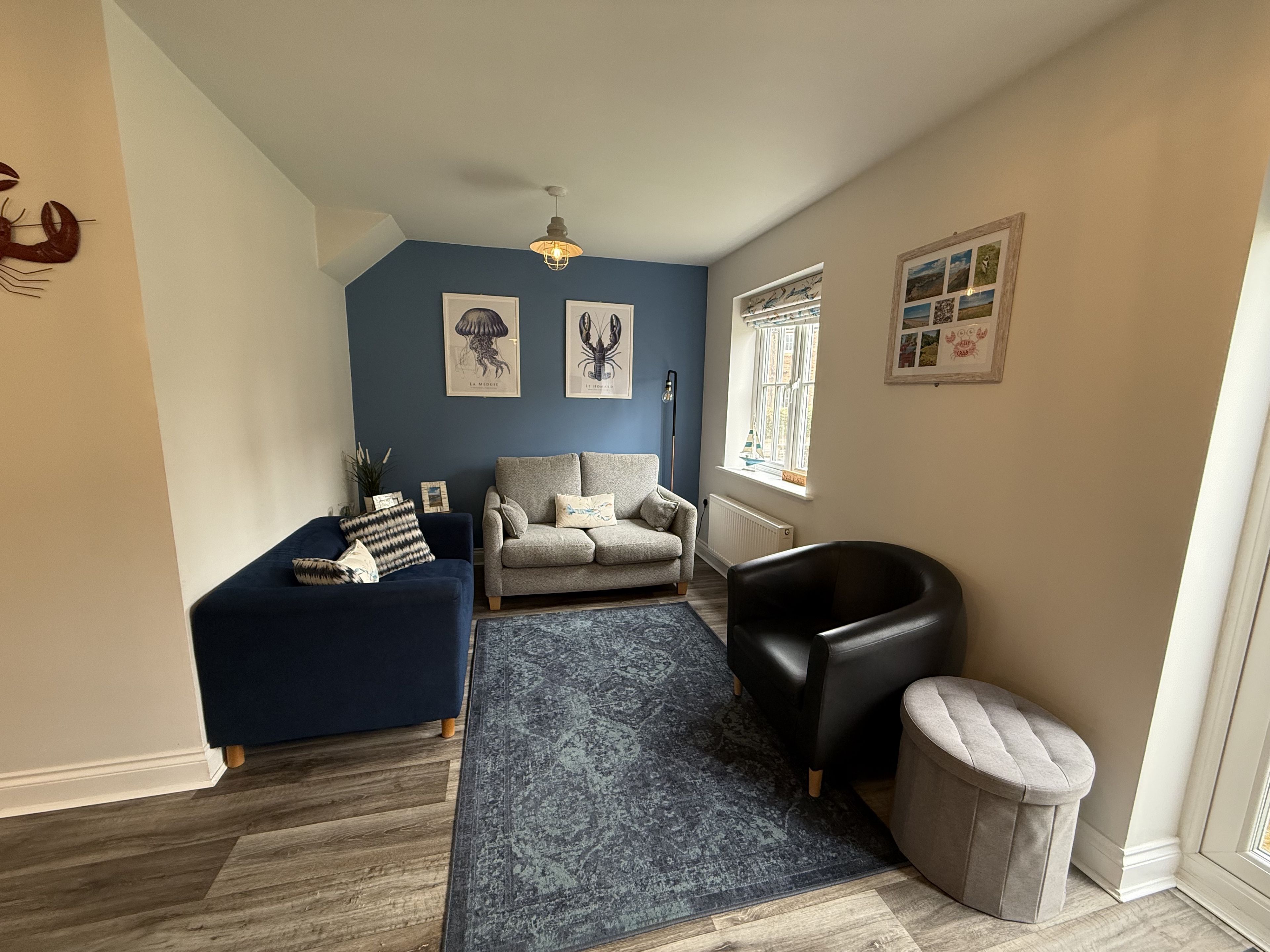 A living room with a blue accent wall, a grey sofa, a black leather chair, and a patterned rug.