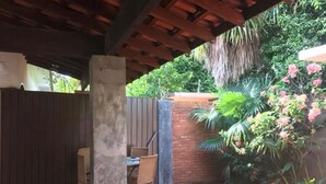 Eine Terrasse im Freien mit Pflasterboden, zwei Korbstühlen, einem Tisch und einer Holz-Pergola.