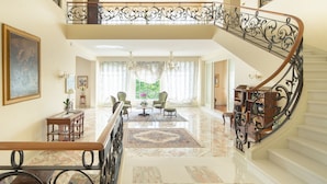Un vestíbulo imponente con suelo de mármol, una escalera con barandillas de metal ornamentadas y un candelabro.