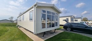 Situated on a well-maintained lawn, this mobile home features a distinctive architectural design with a pitched roof and a front porch.