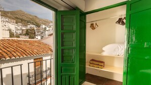 A room with a green door, a balcony with a tiled roof, and a view of a town with white buildings and a mountain in the background. - Casa Sandra, Newly renovated traditional Andalucian townhouse (Competa)