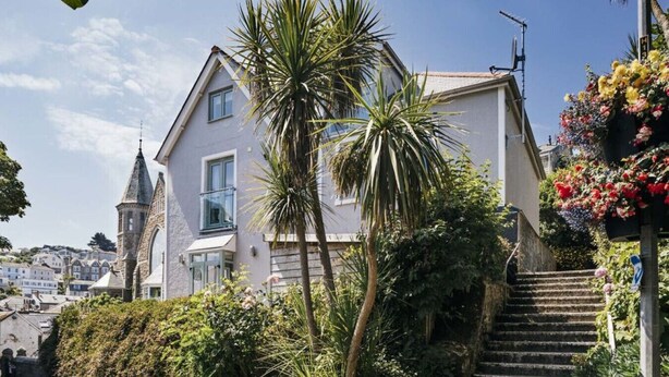 A two-story house with a balcony, surrounded by lush greenery and a clear blue sky. - Luxury Central Apartment With Car Parking (St Ives)