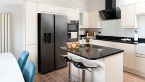 A modern kitchen with a central island, black appliances, and a bar stool. - Luxury Central Apartment With Car Parking (St Ives)