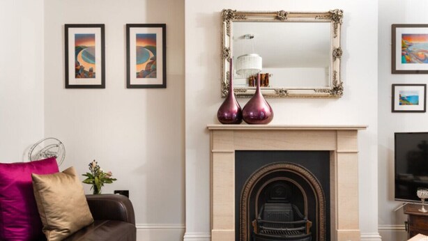 Un salon avec une cheminée, un canapé et une table basse. Des tableaux encadrés ornent le mur et un miroir est placé au-dessus de la cheminée.