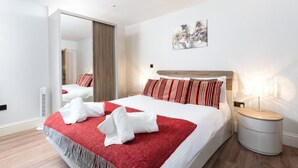 A modern hotel room with a large bed, a bedside table, a mirror, and a painting on the wall. - Luxury Central Apartment With Car Parking (St Ives)