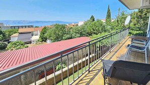 Ein Balkon mit rotem Dach, Metallgeländer und Blick auf Gebäude und Bäume.