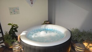 Een hottub met een houten terras, omringd door potplanten en een muur met een bord waarop 'Garden' staat.