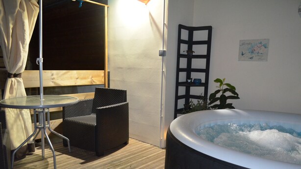 Een bubbelbad, een tafel en twee stoelen in een kamer met een houten vloer en een witte muur.