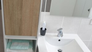 Een badkamer met een wit wastafel, een spiegel en een houten kastje met handdoeken.