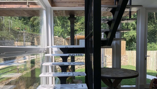 Un interior moderno con un vidrio que da a un patio. En el interior, hay una mesa de madera con un diseño original y varios taburetes con un estampado blanco y negro.