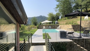 Zona de piscina con muro de piedra, espacio de estar cubierto y vista del paisaje circundante.