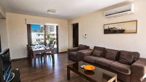 Una sala de estar con un sofá, una mesa de centro y un televisor. Hay un comedor con una mesa y sillas.