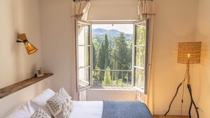 Ein Schlafzimmer mit großem Fenster, einer Nachttischlampe und einem Holzbodenregal.