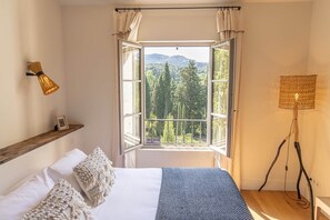 A bedroom with a large window, a bedside lamp, and a wooden shelf. - Bastide du Levant du Mas de l'Amarine (ST REMY DE PROVENCE)