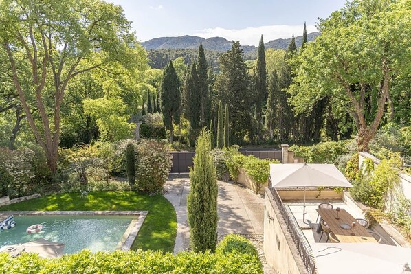 A backyard with a swimming pool, a barbecue area, and a view of mountains.