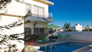 Una piscina amb una escala metàl·lica, envoltada d'un solàrium amb rajoles. Hi ha cadires i un parasol verds a prop de la piscina.