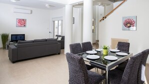 Un saló modern amb un sofà gris, una taula de dinar preparada per a quatre persones i una escala que condueix a un altre pis.