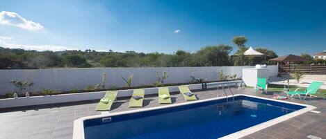A swimming pool with four sun loungers, a covered seating area, and a view of the landscape.
