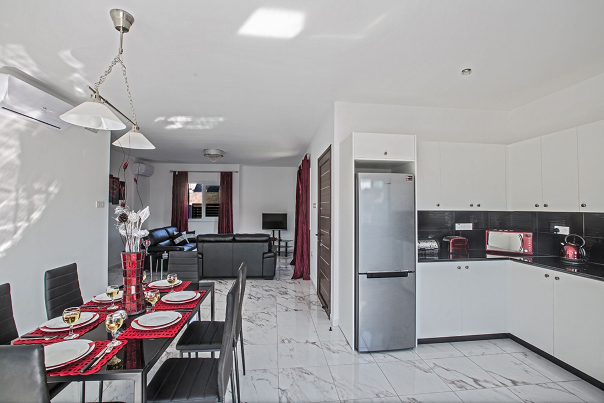 Une cuisine moderne avec des meubles blancs, un réfrigérateur en acier inoxydable et un coin repas avec une table dressée pour quatre personnes.