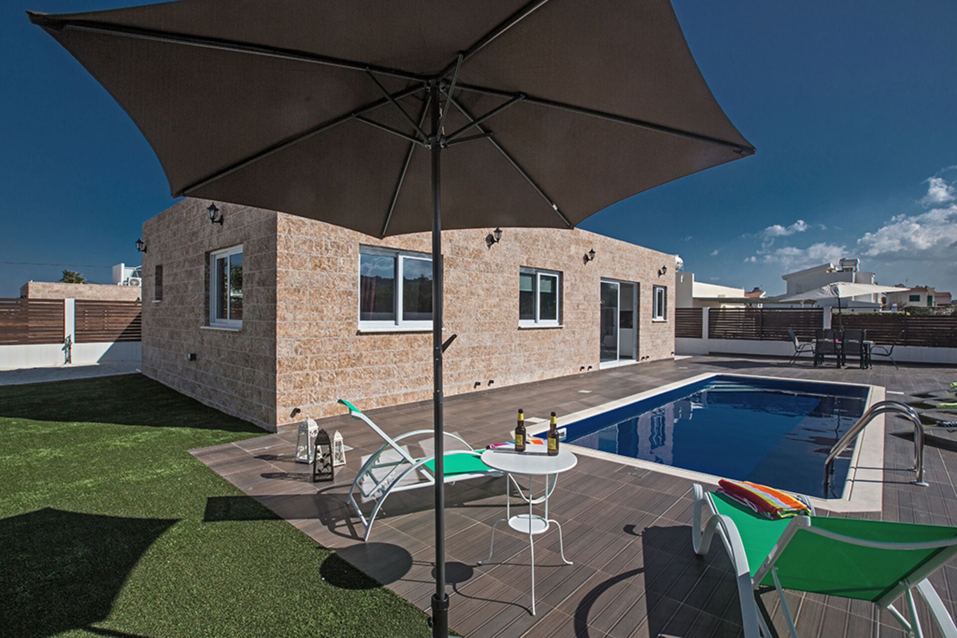 Ein modernes Haus mit Swimmingpool, Gartenmöbeln und einem großen Sonnenschirm.