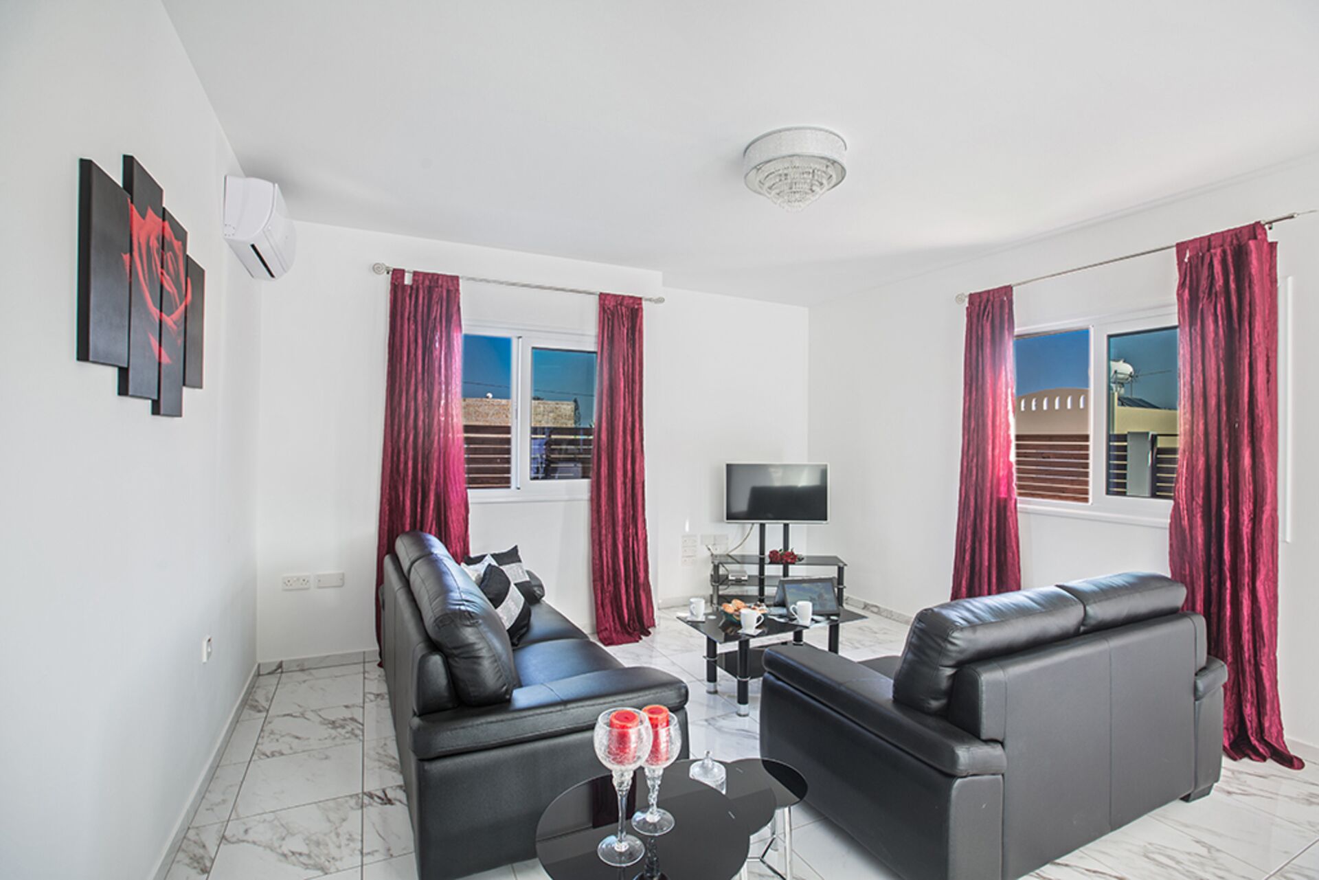 A modern living room with black leather sofas, a flat-screen TV, and a small table with two glasses.