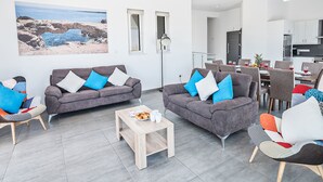 Een moderne woonkamer met twee grijze banken, een houten salontafel en een eethoek met een tafel gedekt voor vier personen.