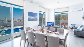 Een moderne woonkamer met een eethoek, grote ramen en uitzicht op het zwembad.