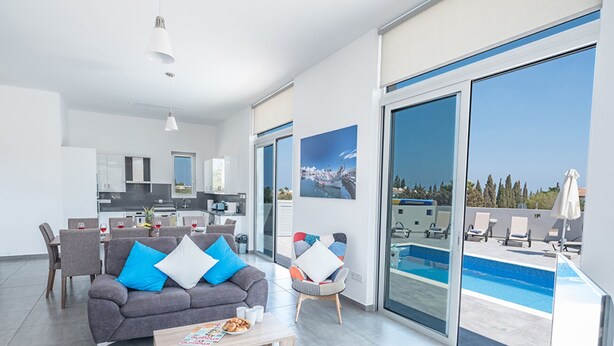 Een moderne woonkamer met een grijze bank, een salontafel en een zwembadgedeelte met loungestoelen en uitzicht op zee.