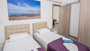 Hotelkamer met twee bedden, een groot raam met uitzicht op het strand, een kledingkast en een airconditioning.